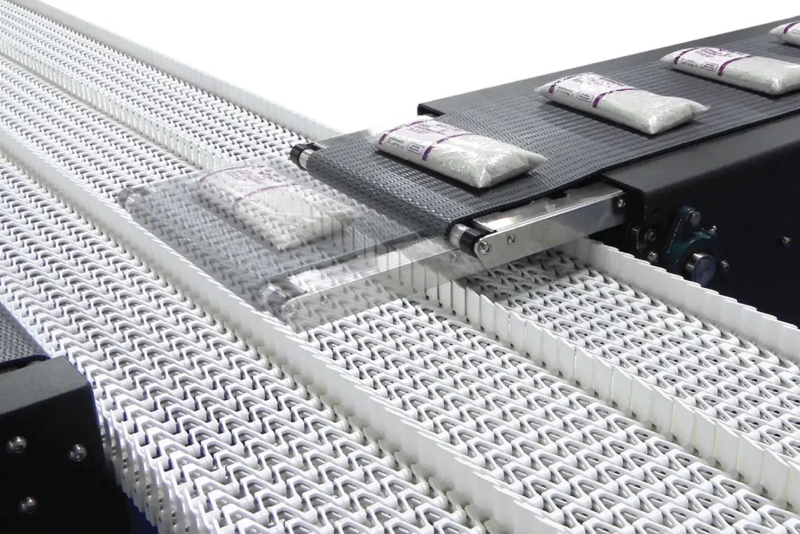 Industrial modular plastic belt conveyor with side transfer moving small sealed pouches across multiple lanes.