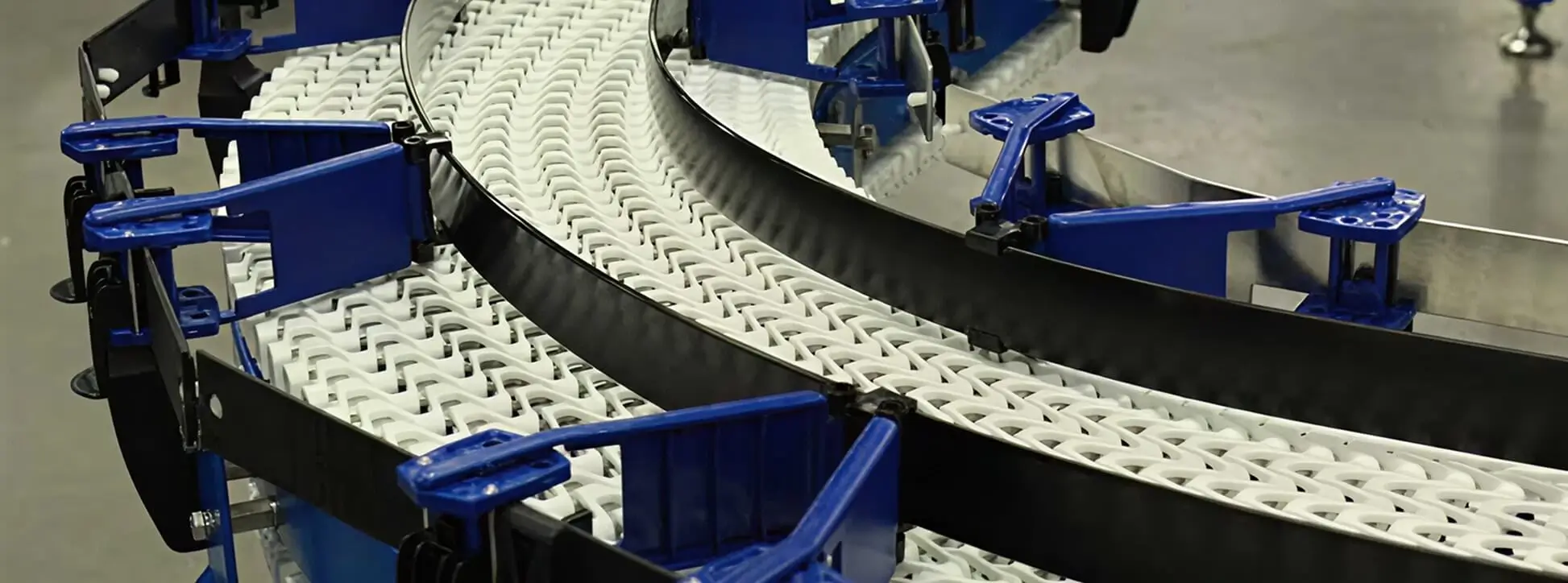 Close-up of EZGUIDE blue tab-lock brackets mounted on a curved Span Tech conveyor with white interlocking chain.