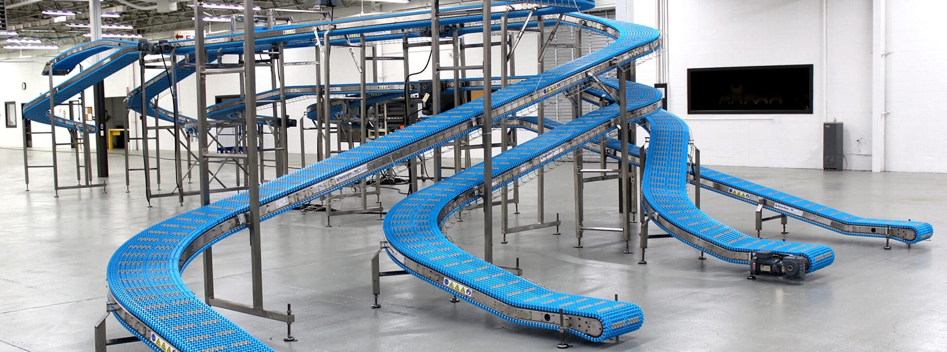cooling-conveyors-for-food-production Blue modular chain conveyor line curving through multiple sections on stainless steel frames in a production facility